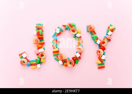 Word Joy aus bunten Süßigkeiten auf einem rosa Hintergrund Stockfoto