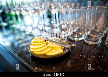 Zitronenscheiben in einer schwarzen Platte werden auf einer Granittheke platziert. Viele Wasser- und Weingläser Hintergründe schaffen schöne Bokeh, elegant und romanti Stockfoto