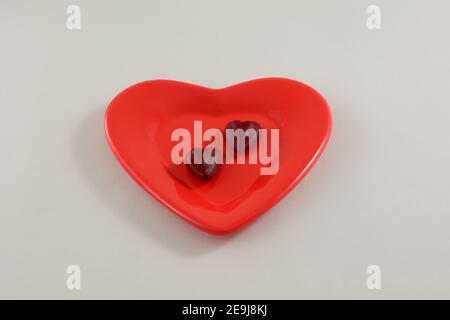 Zwei Bonbons mit Herz aus roter Kirsche am roten Valentinstag Herzförmige Platte auf weißem Hintergrund Stockfoto