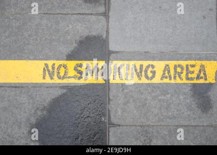Rauchen ist nach dieser Linie verboten. Eine gelbe Linie auf dem Asphalt begrenzt den Nichtraucherbereich auf dem Platz eines Geschäfts- und Geschäftsviertels Stockfoto