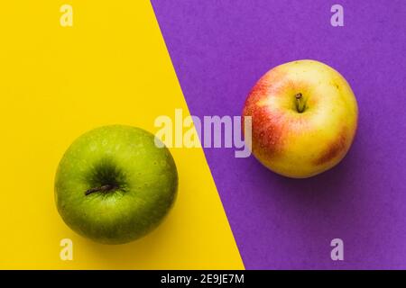 Grüner Apfel und gelb-roter Apfel, auf einem halb violetten und halb gelben Hintergrund Stockfoto