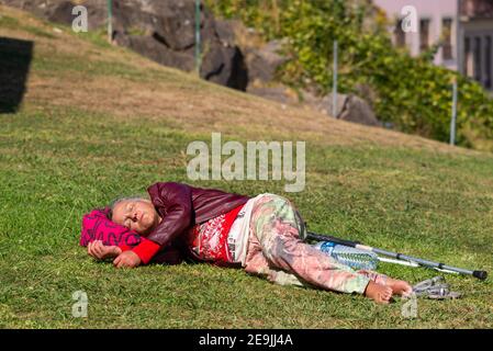 Portugal, Porto, 06. Oktober 2018: Ältere Frau mit Krücken liegt und schlafen auf grünem Gras im Park. Stockfoto