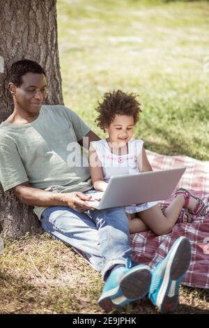 Das kleine Mädchen mit lockigem Haar und ihr Vater sehen sich etwas auf dem Laptop an Stockfoto