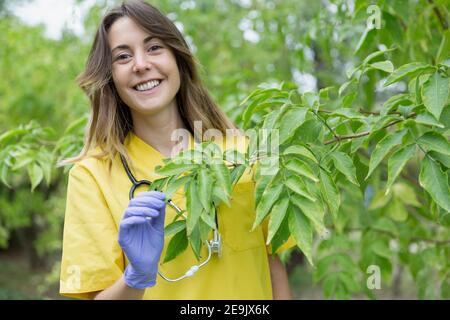 Porträt einer jungen lächelnden Krankenschwester Frau, die sich um Pflanzen in der Natur kümmert. Leerzeichen für Text. Stockfoto