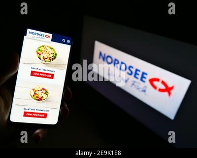 Person, die Smartphone mit Produkten der deutschen Fast-Food-Restaurantkette Nordsee GmbH vor dem Firmenlogo hält. Fokus auf Telefonbildschirm. Stockfoto