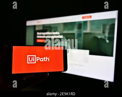 Person mit Handy mit Logo der Software-Entwicklung Firma UiPath Inc. Auf dem Display vor der Business-Homepage. Fokus auf Telefonbildschirm. Stockfoto