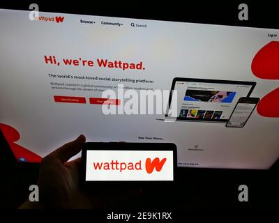 Person hält Smartphone mit Logo der kanadischen Verlags-Website Wattpad auf dem Display vor der Business-Webseite. Fokus auf Telefonbildschirm. Stockfoto