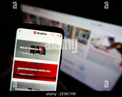 Person mit Smartphone mit Online-Shop des deutschen Großhandelsunternehmens Würth-Gruppe auf dem Display vor der Website. Fokus auf Telefonbildschirm. Stockfoto