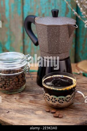 Kaffeekanne zum Brühen von Kaffee auf dem Herd. Tasse Kaffee, Körner in einem Glas. Stillleben am Morgen. Stockfoto