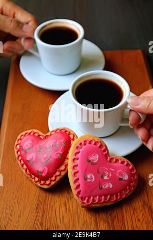 Hände von Frau und Mann halten Tasse Kaffee mit Ein Paar herzförmige Kekse im Vordergrund Stockfoto