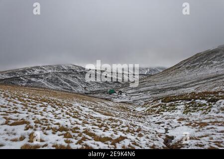 Das Glenshee Ski Center in der Entfernung von den Skipisten im Westen des Resorts, mit Seilbahnmasten, die an der Seite des Cairnwell Mounta laufen Stockfoto