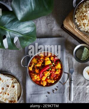 Aloo gobi traditionelle indische Küche aus Blumenkohl und Kartoffeln mit roten Chilischoten, serviert mit braunem Reis, Dahi, Zitronenwasser und Chapati auf der Ta Stockfoto