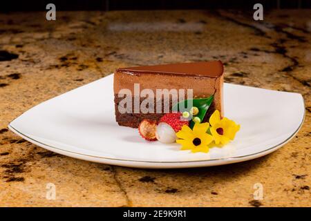 Ein Stück Schokoladenkuchen und Mousse mit gelben Blumen, Litschi auf einem weißen Teller. Stockfoto
