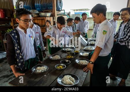 Die Schüler, von denen die meisten Waisenkinder sind, die aus dem Bürgerkrieg geflohen sind, kommen während ihrer Mittagspause in ihr Chinpwi Education Internat in Myikyina, Myanmar. Die Direktorin, Mai WGI Drehhe, verteilt das Essen aus den großen Kochtöpfen. Stockfoto