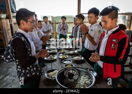 Die Schüler, von denen die meisten Waisenkinder sind, die aus dem Bürgerkrieg geflohen sind, kommen während ihrer Mittagspause in ihr Chinpwi Education Internat in Myikyina, Myanmar. Die Direktorin, Mai WGI Drehhe, verteilt das Essen aus den großen Kochtöpfen. Stockfoto