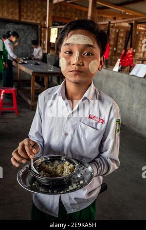 Die Schüler, von denen die meisten Waisenkinder sind, die aus dem Bürgerkrieg geflohen sind, kommen während ihrer Mittagspause in ihr Chinpwi Education Internat in Myikyina, Myanmar. Die Direktorin, Mai WGI Drehhe, verteilt das Essen aus den großen Kochtöpfen. Stockfoto