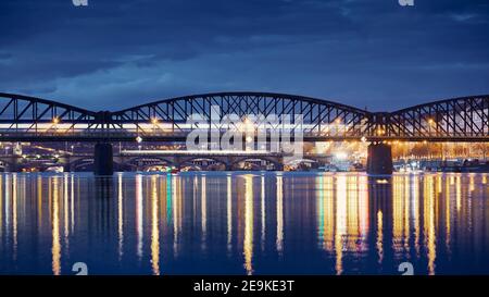 Personenzug, der über die Eisenbahnbrücke gegen die Stadt fährt. Stadtbild von Prag bei Nacht, Tschechische Republik Stockfoto