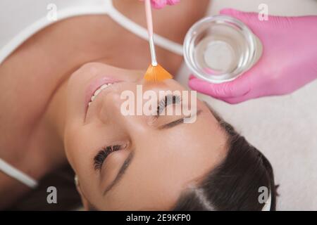 Nahaufnahme von oben Aufnahme einer fröhlichen Frau entspannend Während die Kosmetologin Flüssigpeeling auf ihr Gesicht applyte Stockfoto