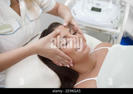 Attraktive Frau lächelt mit geschlossenen Augen und bekommt Gesichtsmassage Stockfoto