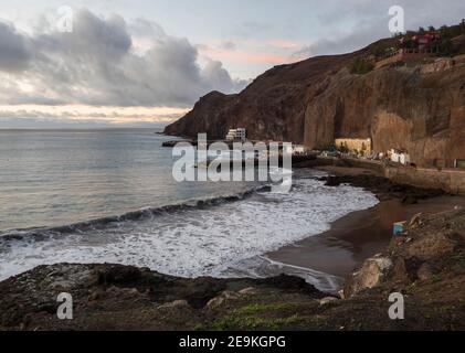 Blick auf das Dorf Puerto de Sardina del Norte mit Sandstrand, Küstenklippen, Yachthafen und bunten Häusern. Grand Canaria, Kanarische Inseln, Spanien. Sonnenuntergang, Stockfoto