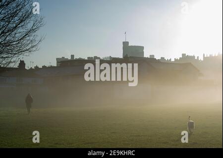 Eton, Windsor, Berkshire, Großbritannien. 5th. Februar 2021. Eine Dame geht mit ihrem Hund auf dem Brocas in Eton im frühen Morgennebel mit Blick auf Windsor Castle. Sonnenschein ist für heute prognostiziert mit Regen und möglicherweise Schnee für das Wochenende. Quelle: Maureen McLean/Alamy Live News Stockfoto