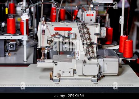 Professionelle multifunktionale und moderne Nähmaschine mit Spulen aus roter Fadennahaufnahme auf dem Hintergrund einer Nähwerkstatt in Blur. Stockfoto