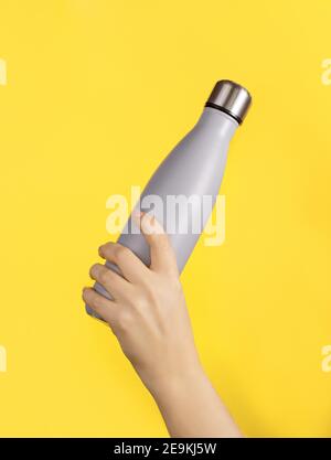 Hand mit grauer wiederverwendbarer Isolierflasche auf gelbem Hintergrund. Zero Waste, plastikfreies und nachhaltiges Lifestyle-Konzept Stockfoto