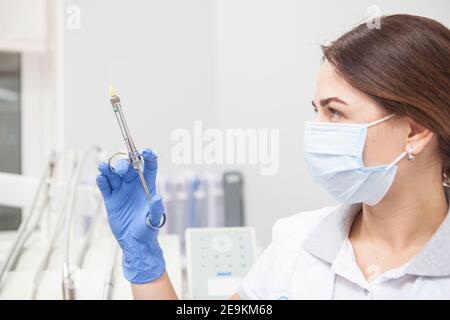 Nahaufnahme einer Ärztin, die eine medizinische Gesichtsmaske trägt und die Spritze anschaut, die sie hält Stockfoto