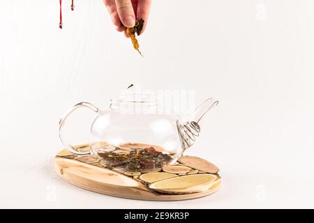 Eine weibliche Hand gießt chinesischen aromatischen Kräutertee in ein Glas Teekanne steht auf einem hölzernen Ständer auf einem weißen Holztisch Stockfoto