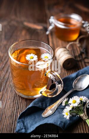 Kräutermedizin für die Gesundheit der Atemwege, eine Tasse Gänseblümchen-Tee mit Honig auf rustikalem Holzhintergrund Stockfoto