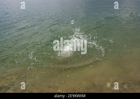 Spritzer, Wellen, Kreise, die von Steinen ins Meer geworfen, Tropfen von frischem, hellem Wasser, Rauschen, Splash. Wellen auf Meer abstraktes Texturmuster. Stockfoto