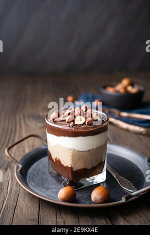 Lagendessert mit Schokoladenmousse, Frischkäse und Schlagsahne gemischt mit Kastanienpüree, garniert mit Haselnüssen in einem Glas auf rustikalem Holz Stockfoto