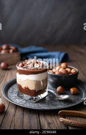 Lagendessert mit Schokoladenmousse, Frischkäse und Schlagsahne gemischt mit Kastanienpüree, garniert mit Haselnüssen in einem Glas auf rustikalem Holz Stockfoto