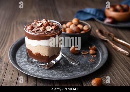 Lagendessert mit Schokoladenmousse, Frischkäse und Schlagsahne gemischt mit Kastanienpüree, garniert mit Haselnüssen in einem Glas auf rustikalem Holz Stockfoto