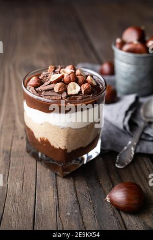 Lagendessert mit Schokoladenmousse, Frischkäse und Schlagsahne gemischt mit Kastanienpüree, garniert mit Haselnüssen in einem Glas auf rustikalem Holz Stockfoto