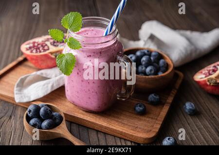 Granatapfel und Heidelbeer-Smoothie gemischt mit Joghurt und Mandelmilch, serviert in einem Glas auf rustikalem Holzhintergrund Stockfoto