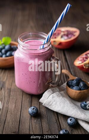 Granatapfel und Heidelbeer-Smoothie gemischt mit Joghurt und Mandelmilch, serviert in einem Glas auf rustikalem Holzhintergrund Stockfoto