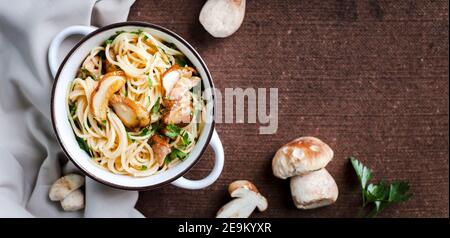 Pasta mit frischen Steinpilzen und Petersilie in einem weißen Vintage Topf auf einer braunen Tischdecke Stockfoto