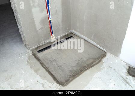 Ein moderner schwarzer linearer Duschabfluss im Duschboden, sichtbare Wasserleitungen in der Wand. Stockfoto