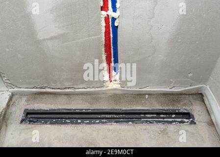 Ein moderner schwarzer linearer Duschabfluss im Duschboden, sichtbare Wasserleitungen in der Wand. Stockfoto