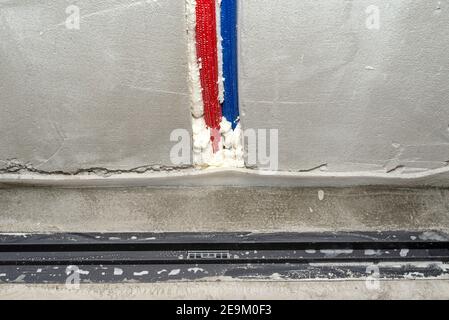 Ein moderner schwarzer linearer Duschabfluss im Duschboden, sichtbare Wasserleitungen in der Wand. Stockfoto