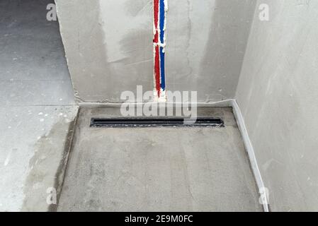 Ein moderner schwarzer linearer Duschabfluss im Duschboden, sichtbare Wasserleitungen in der Wand. Stockfoto