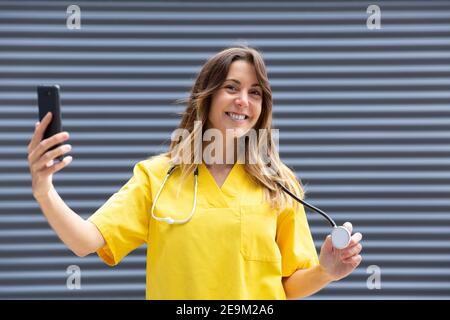 Junges lächelndes Mädchen, das ein Foto mit ihrem Handy machte, während es als Krankenschwester arbeitete. Leerzeichen für Text. Stockfoto