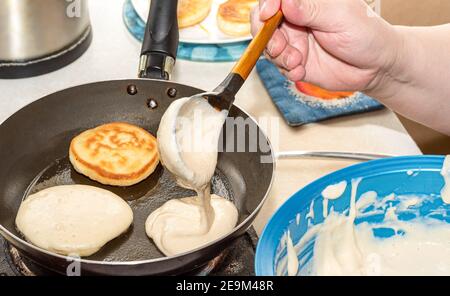 Die Frau gießt den Teig in eine heiße Pfanne. Kochen Pfannkuchen zu Hause. Nahaufnahme. Stockfoto
