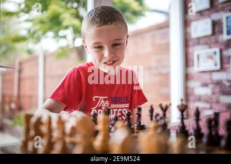 Glücklicher Junge in hellen und luftigen Zimmer lächelt glücklich Spaß beim Schachspielen mit Brett und Stücke in Sicht arbeiten Raus aus nächster Bewegung Außenansicht Stockfoto
