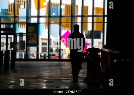 Silhouette des erwachsenen Mann zu Fuß weg von hellen bunten modernen Krankenhaus in der Nacht in der Dunkelheit mit weißen großen Fensterleuchten Hinter ihm Stockfoto