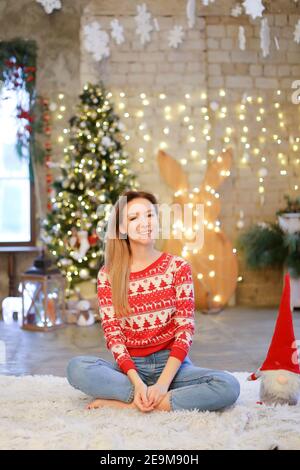 Kaukasische blonde Mädchen sitzt auf Decke mit Weihnachtsbaum im Hintergrund. Stockfoto