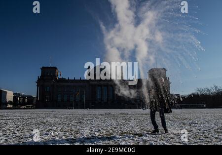 Berlin, Deutschland. Januar 2021, 31st. Auf dem Rasen vor dem Reichstag schleudert ein Mann kochendes Wasser aus einer Flasche in die Luft, die bei den Temperaturen unter dem Nullpunkt sofort friert. Quelle: Paul Zinken/dpa-Zentralbild/ZB/dpa/Alamy Live News Stockfoto