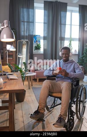 Afrikanischer behinderter Mann, der im Rollstuhl sitzt und sein Handy benutzt Telefonieren, während Sie zu Hause sitzen Stockfoto