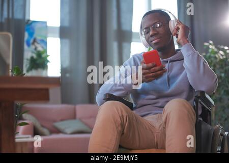 Glücklicher afrikanischer Mann, der auf dem Rollstuhl sitzt und etwas auf dem Handy beobachtet Telefon und Lächeln Stockfoto